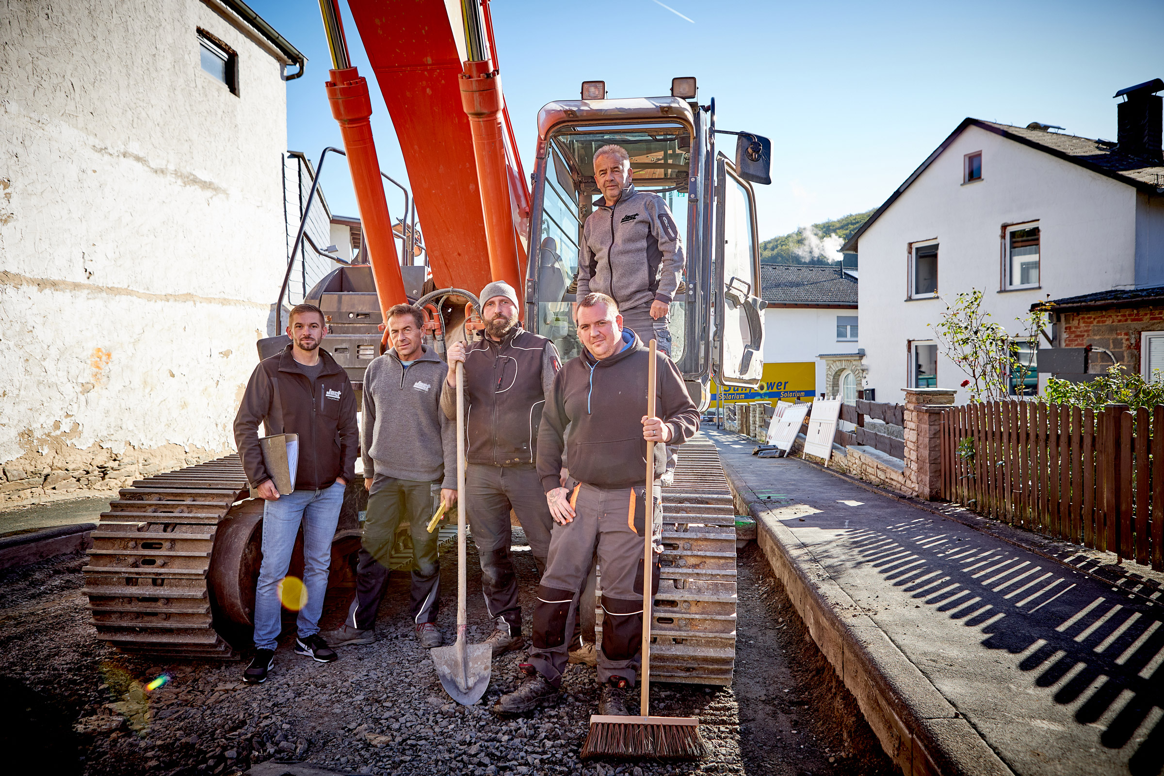 Das Jost-Team auf einer Straßenbau Baustelle vor einem Bagger
